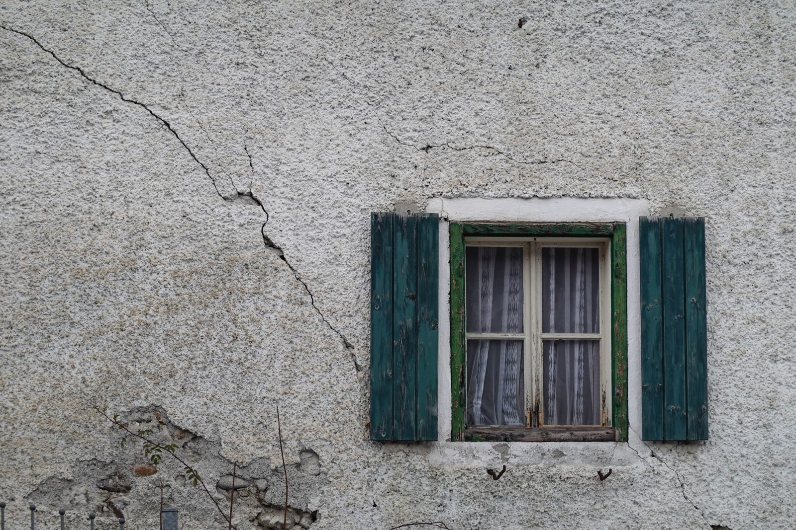Verputzte Hauswand mit Riss neben einem Fenster mit grünen Fensterläden